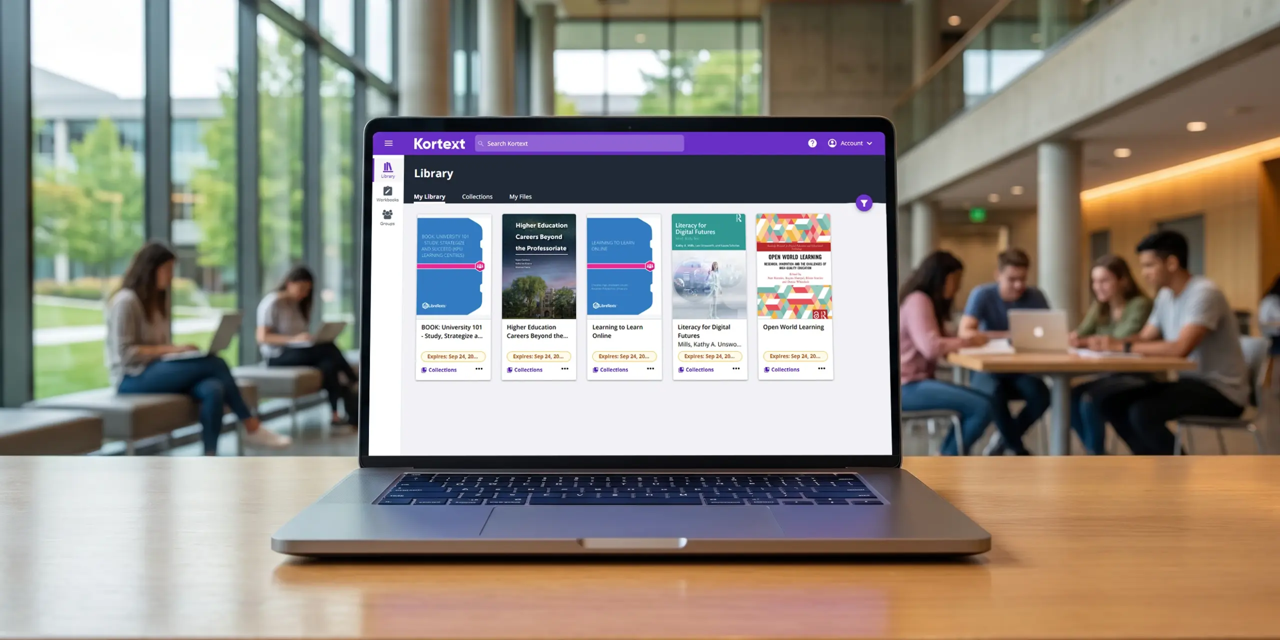A laptop displaying the Kortext library in an academic library with students studying in the background.