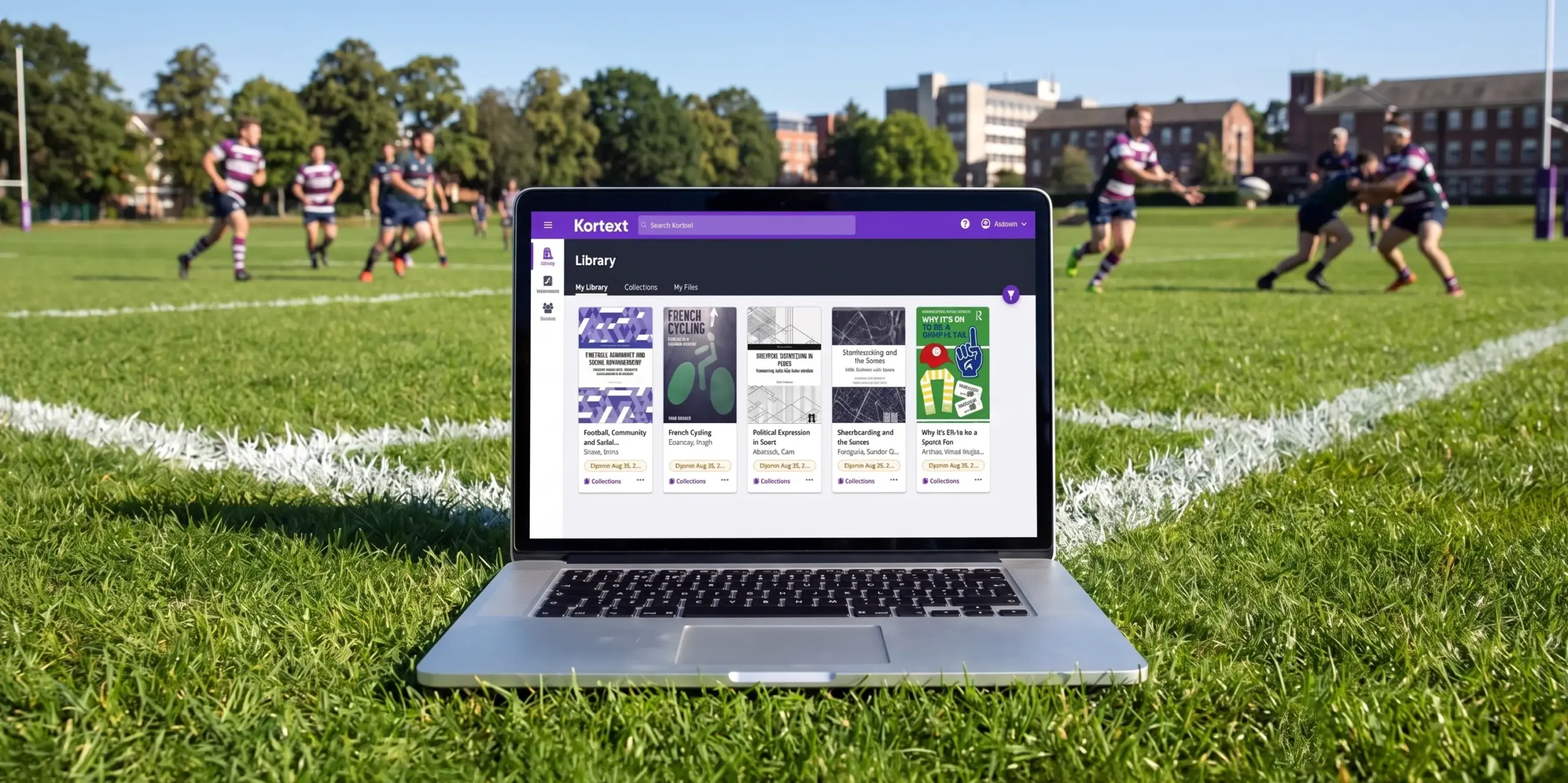 A laptop displaying the Kortext library sits on a rugby pitch, with players running a match in the background behind it.
