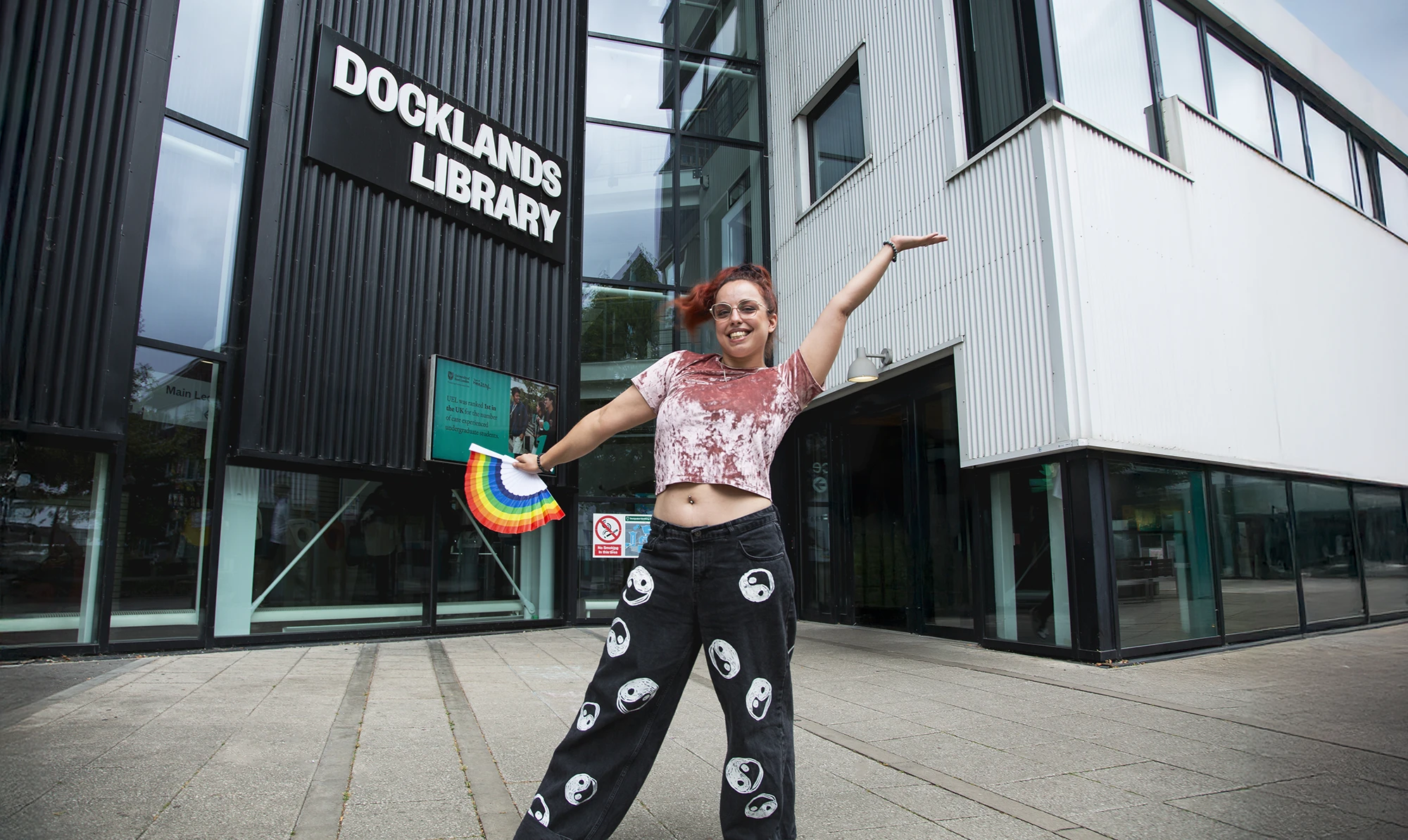 Darya Ashrafi, UEL student and Kortext student ambassador, standing outside Docklands Library holding a rainbow fan