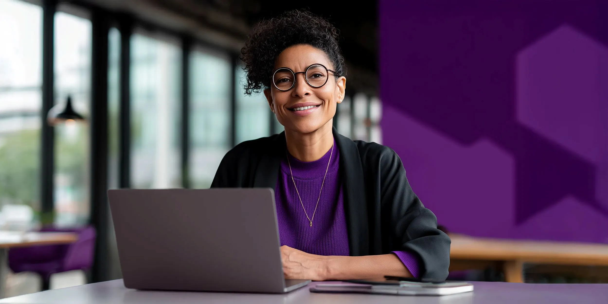 Person sitting at a desk with a laptop, smiling in a modern office environment.